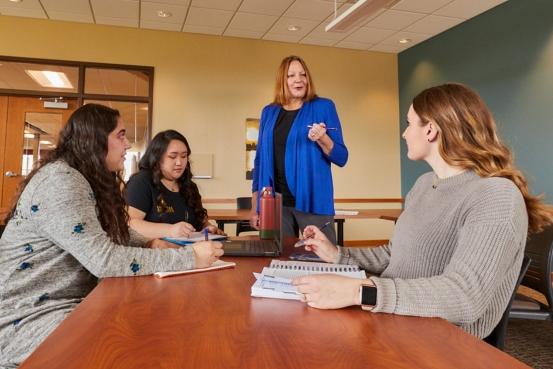 Group of three students sitting in a classroom at a table listening to professor teach